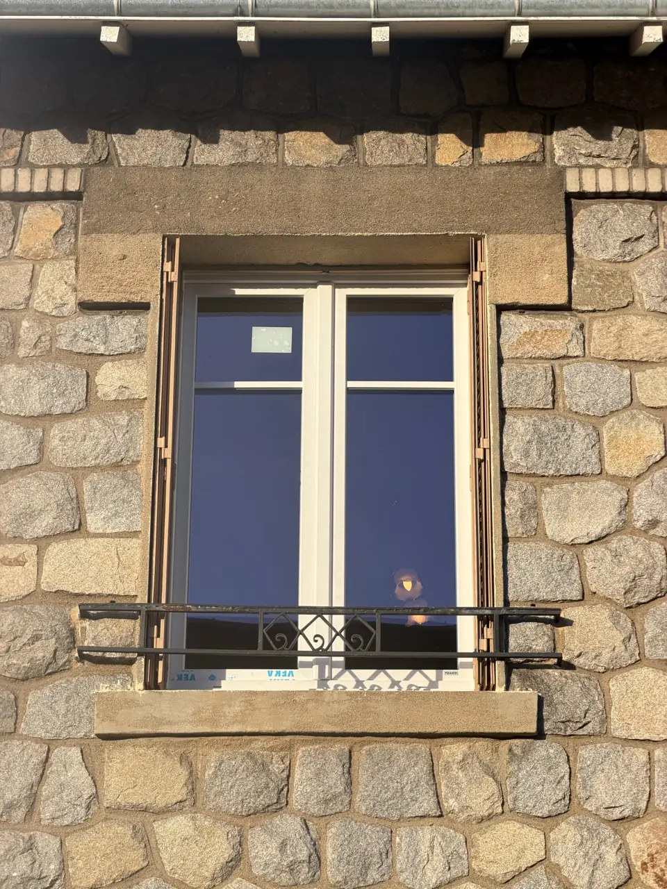 Fenêtre en bois avec balcon en métal sur façade en pierre.