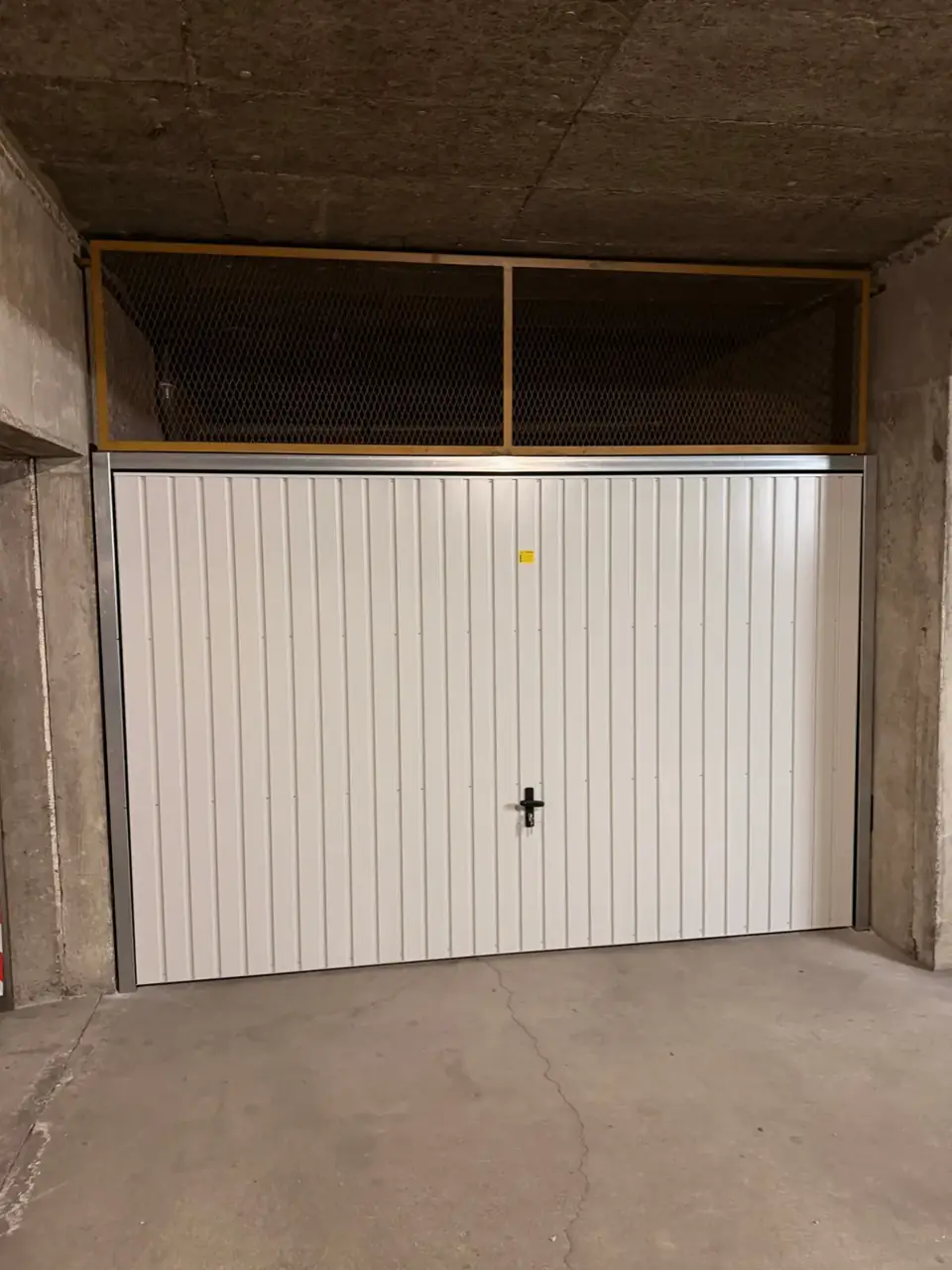 Portail de garage en PVC blanc avec serrure et ventilation.