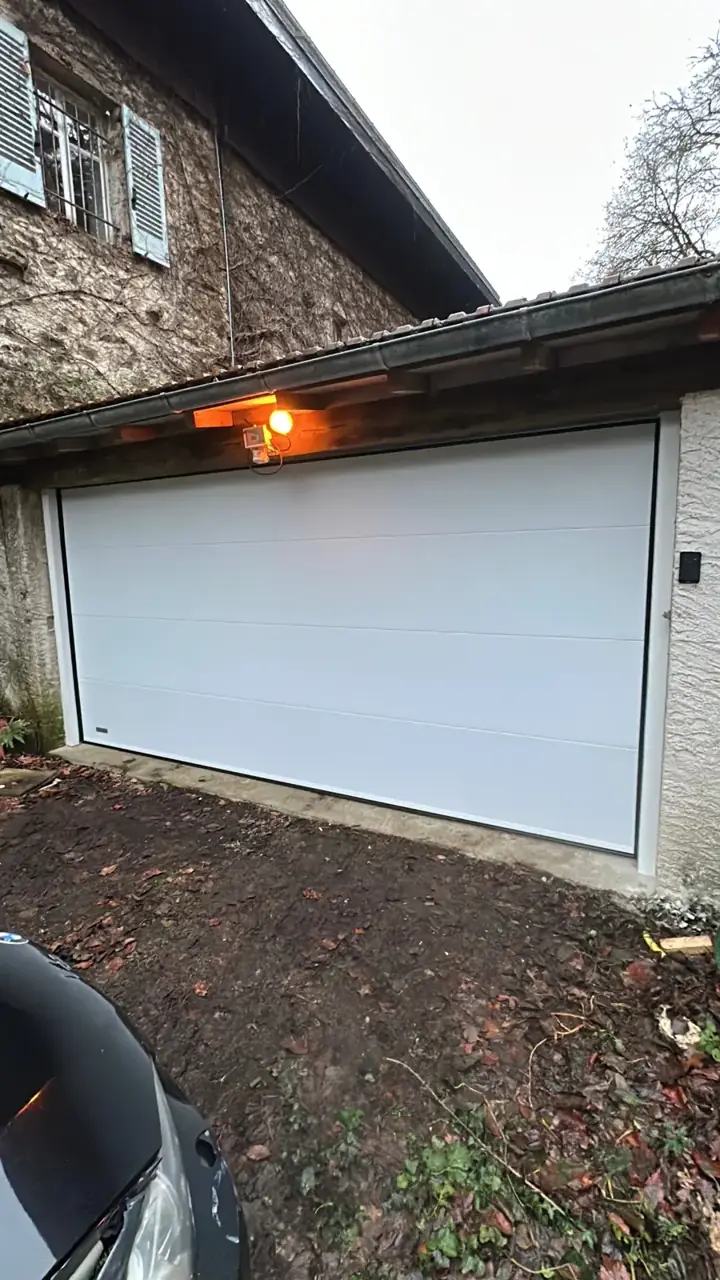 Portail de garage blanc en PVC avec motorisation et éclairage extérieur.