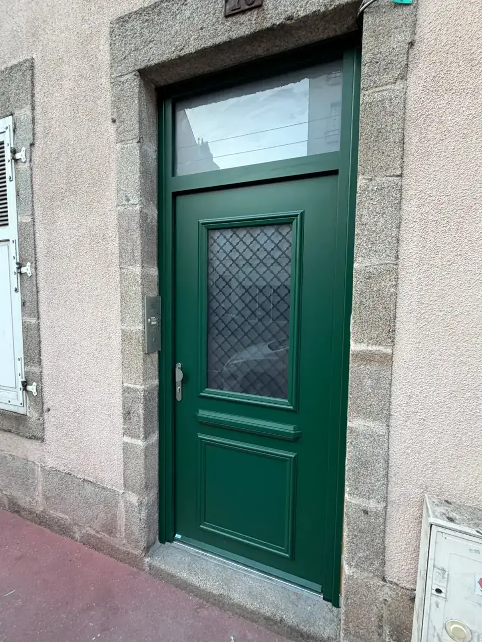 Porte en bois vert avec fenêtre en verre et motif en treillis.